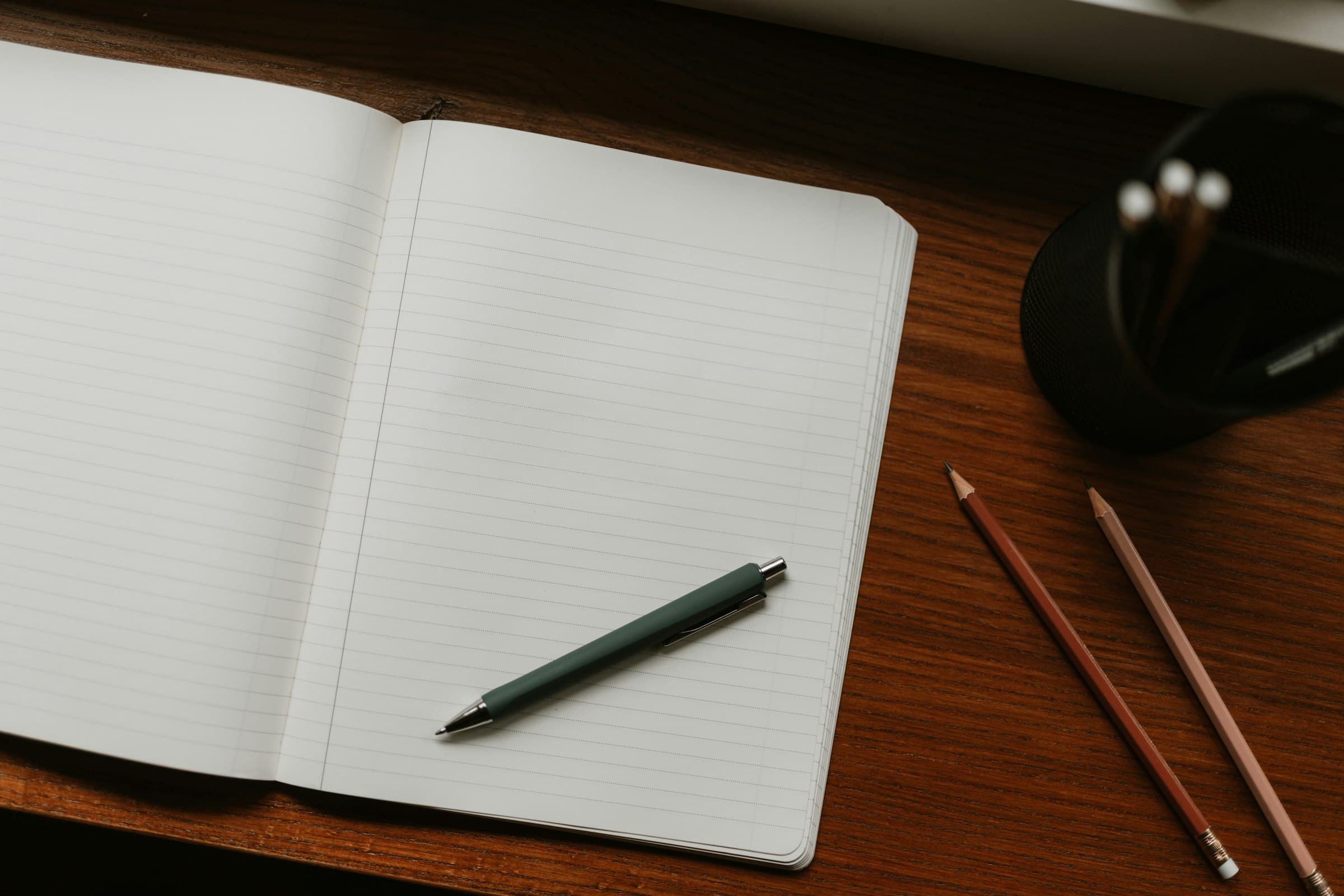 An open notebook with a pen and pencils on a desk